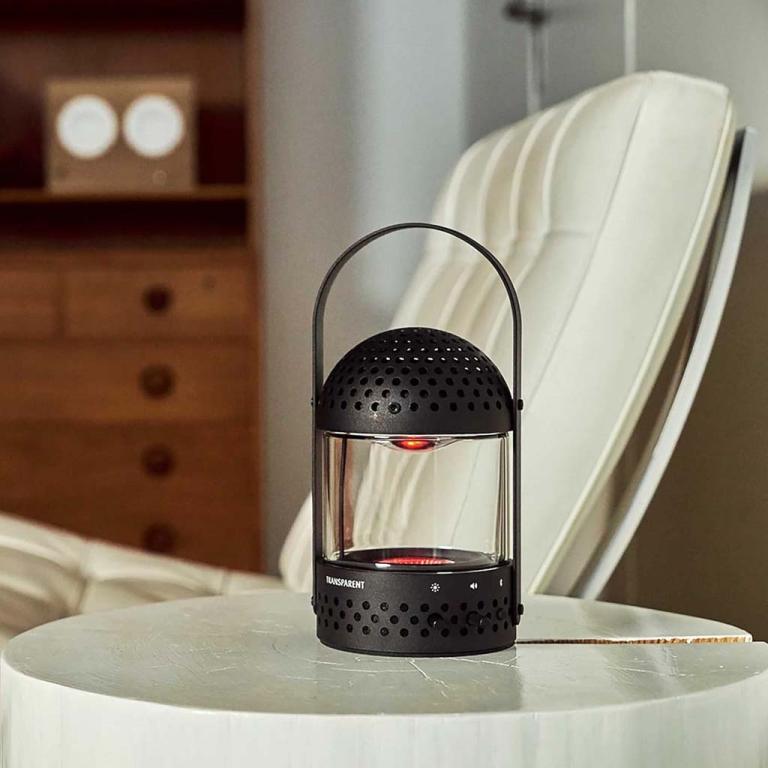 The black variant of the Light Speaker from Transparent, set on a side table besides a white chair